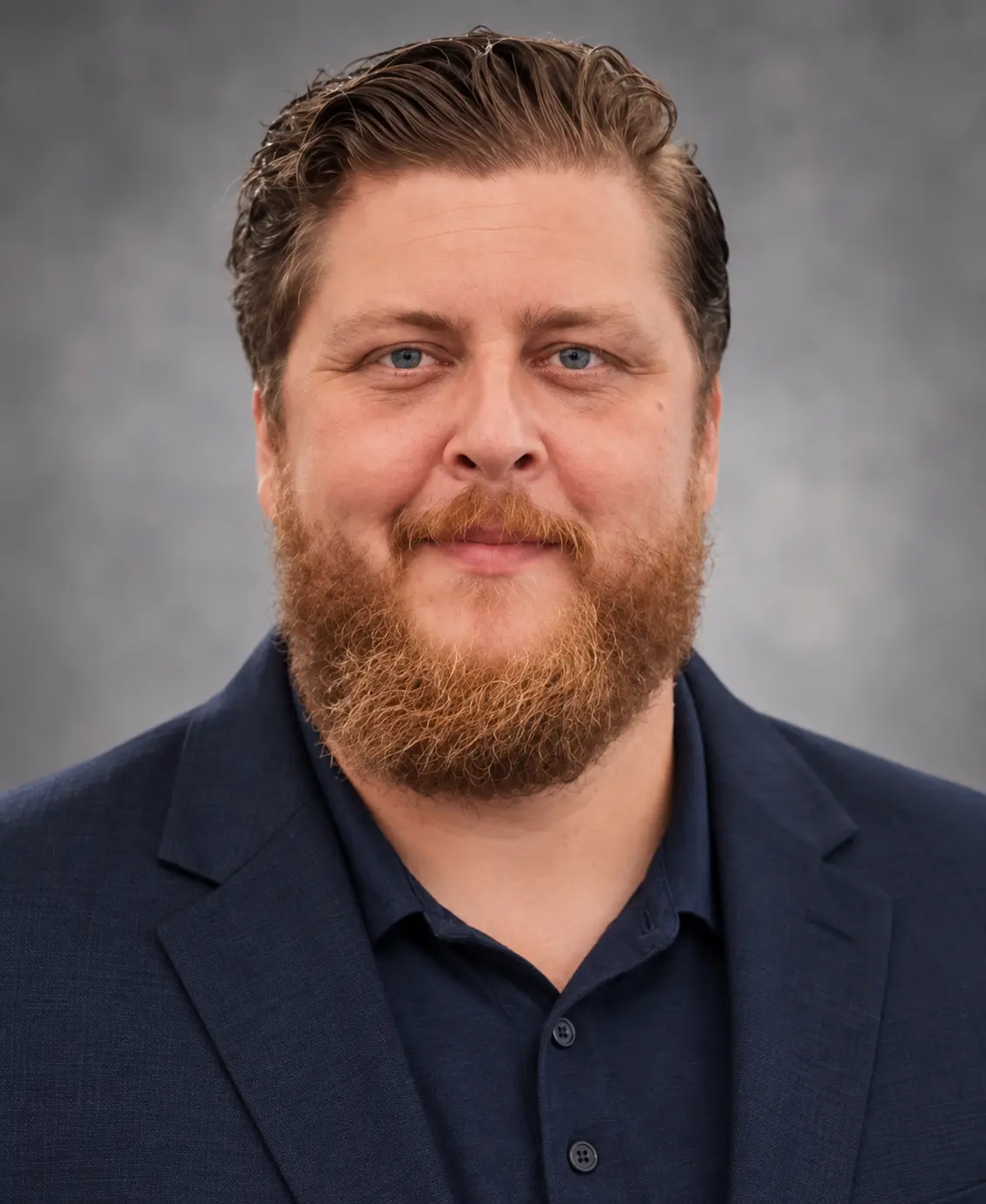 Bearded man in navy blazer against gray background