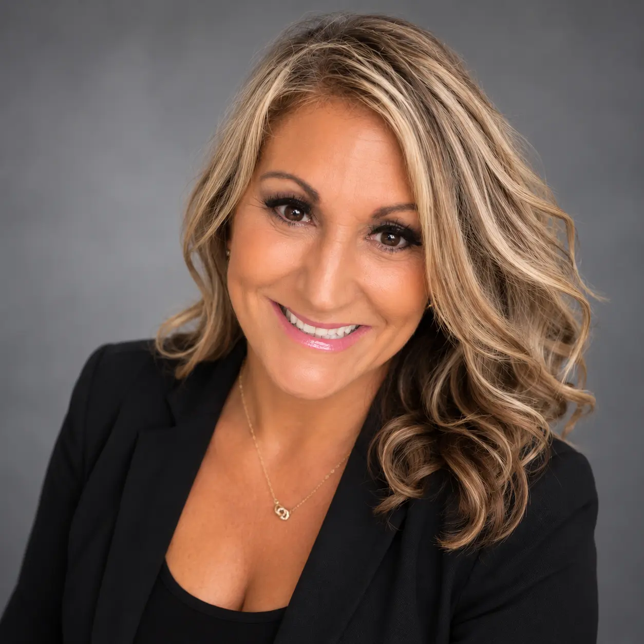 Smiling blonde woman in black blazer against gray backdrop