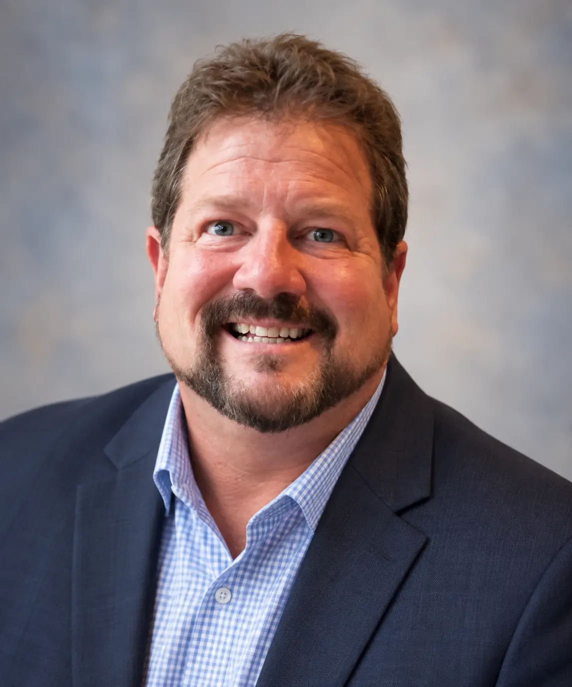 Smiling man in a navy blazer and checkered shirt
