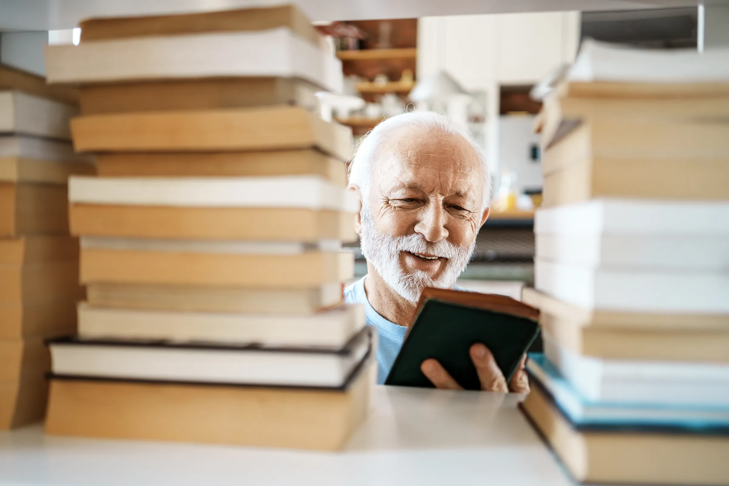 Smiling elderly man reading book between tall stacks