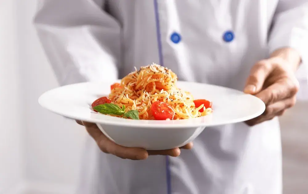 Chef presenting spaghetti with tomatoes, basil, and grated cheese